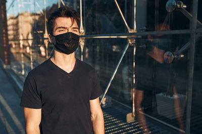 Young man walking in the city center along glass store front in the evening, looking away