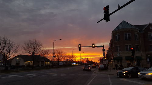 Cars on street by buildings against sky during sunset