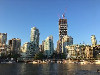 Modern buildings by river against clear sky