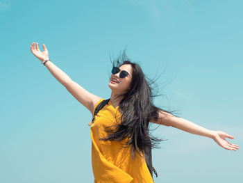 Young woman wearing sunglasses standing against sky