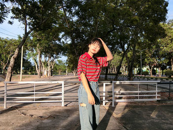 Young woman standing on railing against trees