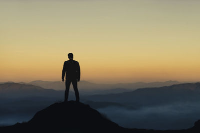 Rear view of silhouette man standing on mountain against sky during sunset