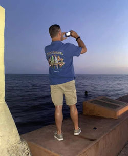 Rear view of man photographing sea against sky