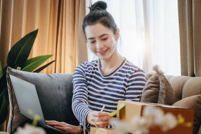 Young woman using phone while sitting on sofa at home