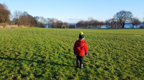 Rear view of child walking on grassy field during sunny day