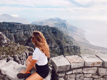 Woman sitting on mountain against sky