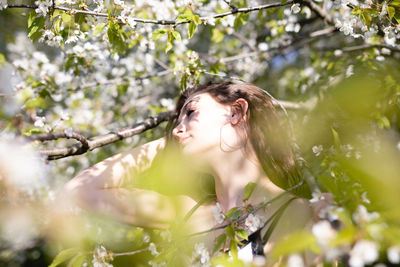 Thoughtful young woman looking away while standing by plants in park