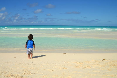 Rear view of boy on beach against sky