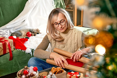 Blond woman wrapping presents in recycled card and decorated it with dried oranges and fir branches.