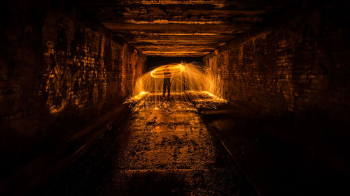 Man spinning illuminated wire wool in tunnel at night