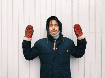 Portrait of man in warm clothing standing with arms raised against wall