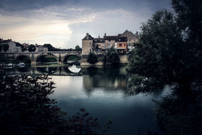 Bridge over river by houses against sky