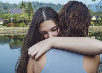 Close-up of smiling daughter embracing mother while standing outdoors