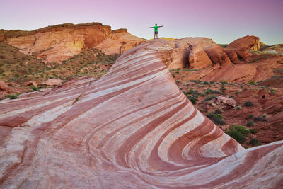 Distant view of man standing on rock formations during sunset
