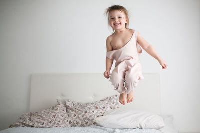 Happy funny girl toddler life style with a smile jumping on the bed, the concept 