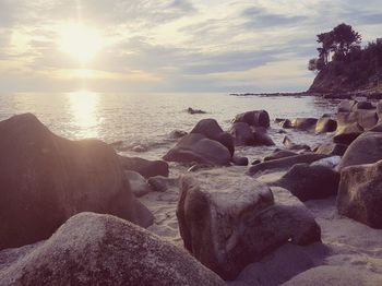 Rocks on beach against sky during sunset