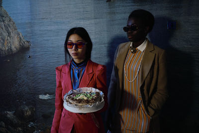 Woman holding food while standing with friend against poster