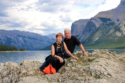 Portrait of couple sitting on rock formation against mountains