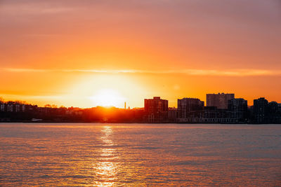 Sea by buildings against sky during sunset