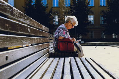 Senior woman writing in paper while sitting on bench