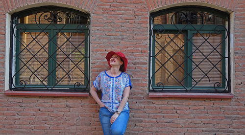 Smiling woman looking up while standing against brick wall