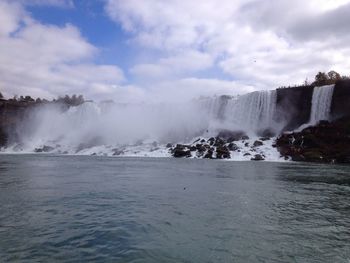 Scenic view of waterfall against cloudy sky