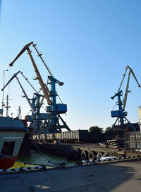 Cranes at harbor against clear blue sky