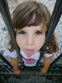 Close-up portrait of cute girl sticking out tongue while standing at railing