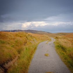 Road passing through landscape against cloudy sky