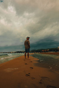 Rear view of man standing on beach against sky