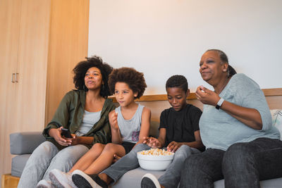 Family watching tv while sitting on sofa at home