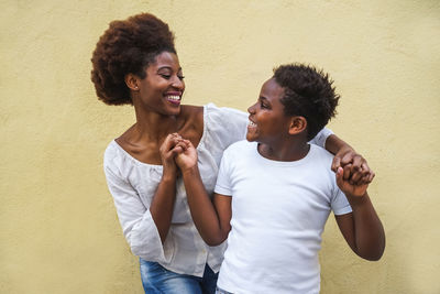 Smiling siblings standing against wall