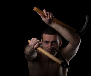 Portrait of shirtless man holding weapons against black background