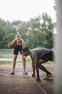 Female coach assisting man preparing for sprint on running track