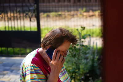 Old lady with wrinkled skin call and speaking touchscreen smartphone. nature background, close up,