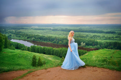 Pregnant woman in blue dress, green hills, river and sky