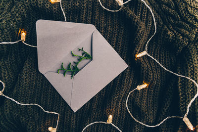High angle view of string lights by envelope with leaves on woolen fabric