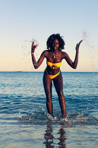 Full length of man splashing water in sea against sky