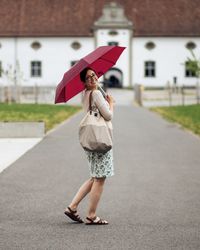 Full length of woman with umbrella standing on road