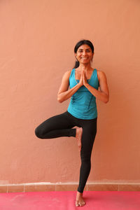 Portrait of smiling young woman standing against wall in a yoga pose