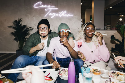 Portrait of happy multiracial male and female friends with props having food in college dorm