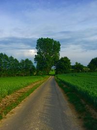 Empty road amidst field against sky