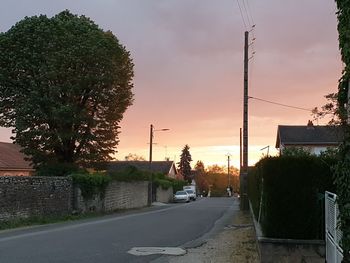 Road by trees against sky during sunset