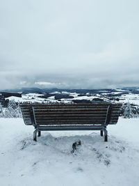 Empty bench on snow covered field against clear sky