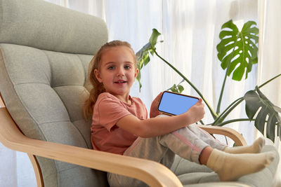 Cute child showing mobile phone while sitting on armchair