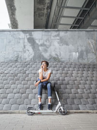 Woman talks by smartphone. female on grey tiled wall background. eco-friendly urban transport.