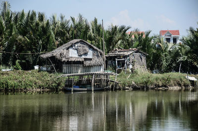 House by lake against trees and sky