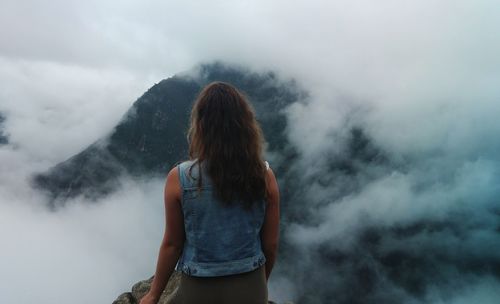 Rear view of woman looking at mountains during foggy weather