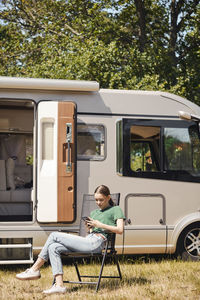 Teenage girl using mobile phone while sitting on folding chair by camper van