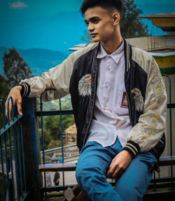 Young man looking away while standing against railing